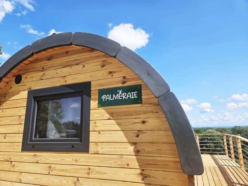 Cabane en bois "Palmeraie" avec vue dégagée sur la nature et ciel bleu.