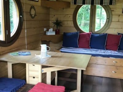 Intérieur d'un chalet en bois avec de grandes fenêtres rondes et un coin salon confortable.