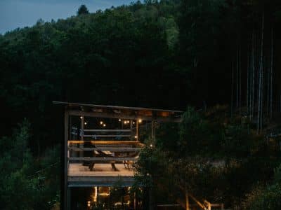 Cabane en bois suspendue, illuminée par des lanternes, entourée de verdure et de forêt.
