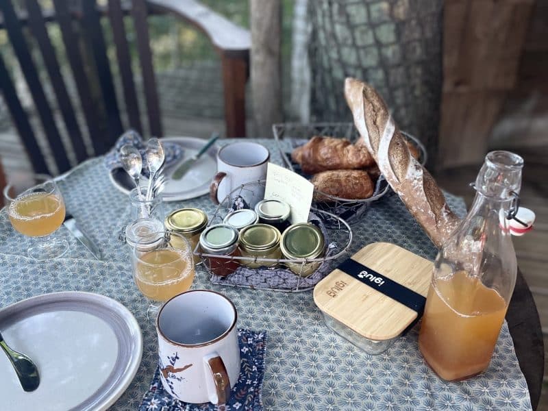 Table en bois dans une cabane perchée, avec petit-déjeuner gourmand et boissons.