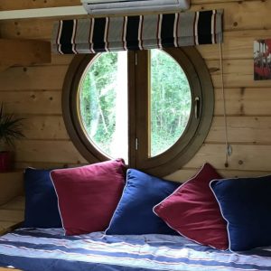 Un charmant cabanon en bois avec un grand rond de fenêtre et des coussins colorés.