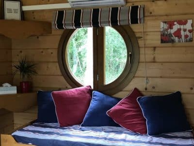 Un charmant cabanon en bois avec un grand rond de fenêtre et des coussins colorés.