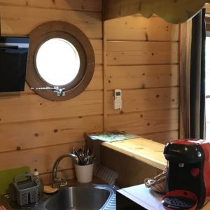 Intérieur d'un chalet en bois avec cuisine équipée et fenêtre ronde, ambiance chaleureuse.