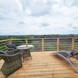 Terrasse en bois d'une cabane perchée, avec vue panoramique sur la nature environnante.