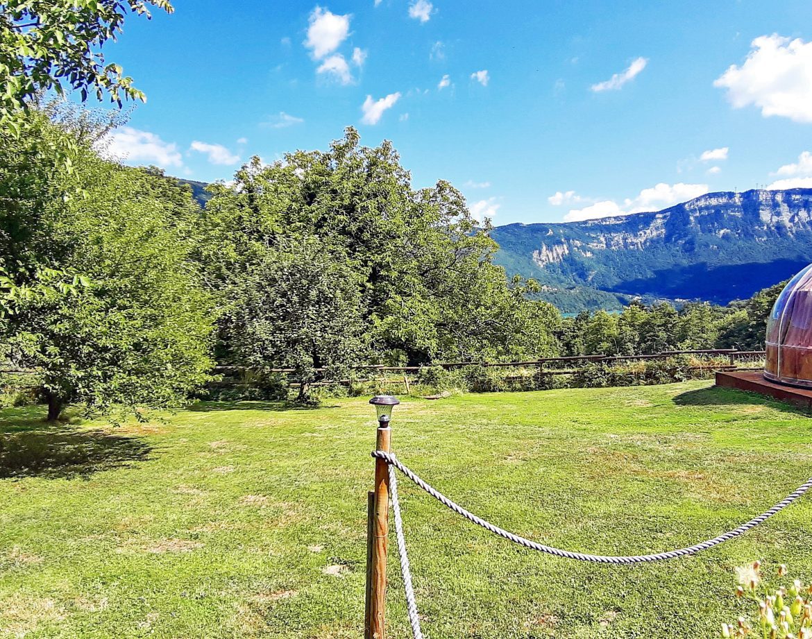 Hébergement insolite : bulle transparente sur un terrain verdoyant avec vue sur les montagnes.