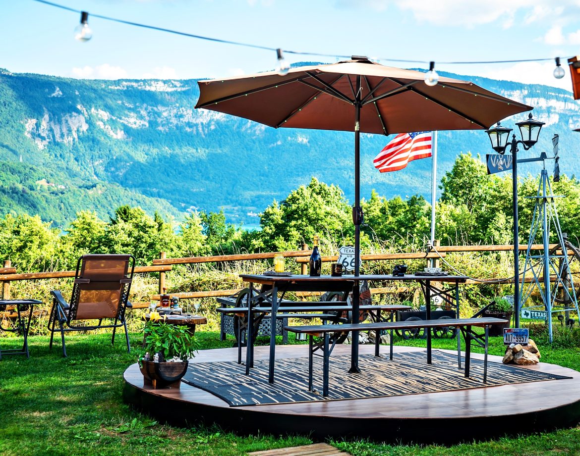 Espace extérieur d'un chalet avec parasol, vue sur les montagnes et drapeau flottant.