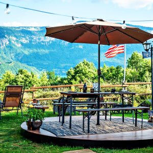 Espace extérieur d'un chalet avec parasol, vue sur les montagnes et drapeau flottant.