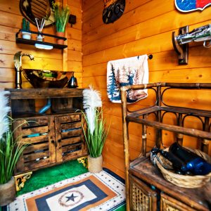 Cabane en bois avec décor rustique, lavabo en cuivre et touches de verdure. Ambiance chaleureuse.