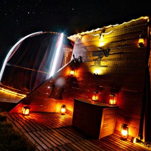 Hébergement insolite : une cabane en bois illuminée sous un ciel étoilé, ambiance chaleureuse.