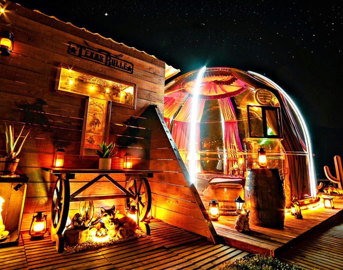 Hébergement insolite : bulle transparente illuminée, décorée de lanternes et d'éléments rustiques.