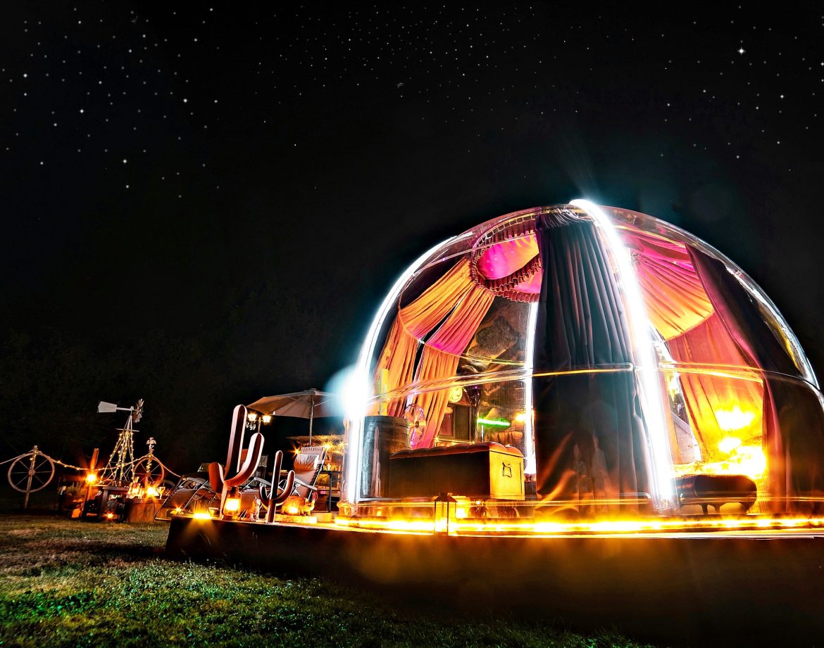 Dôme transparent illuminé sous un ciel étoilé, offrant une expérience unique en pleine nature.