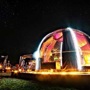 Dôme transparent illuminé sous un ciel étoilé, offrant une expérience unique en pleine nature.