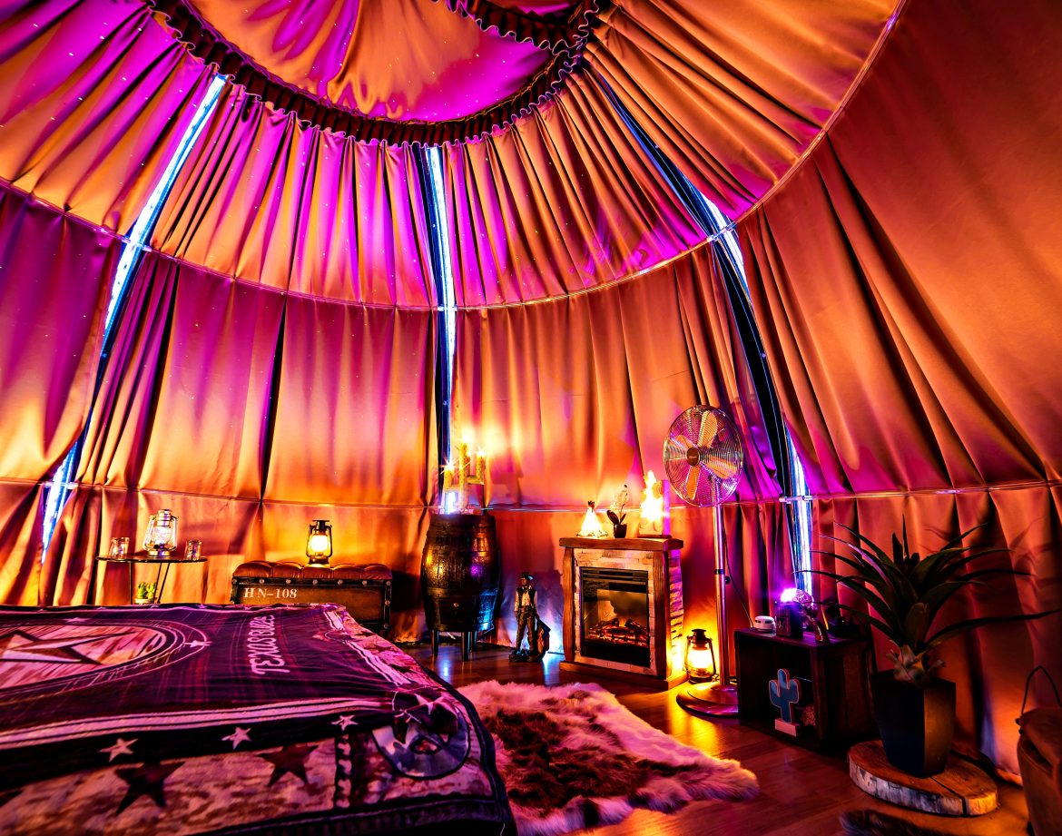 Tente de glamping colorée avec un lit douillet, éclairage tamisé et décor chaleureux.