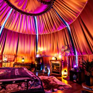 Tente de glamping colorée avec un lit douillet, éclairage tamisé et décor chaleureux.