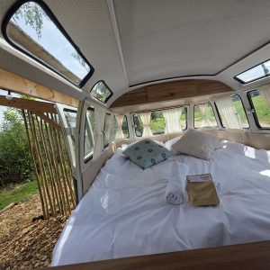 Chambre dans un van vintage, lit spacieux avec vue sur la nature et lumière naturelle.