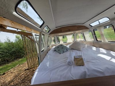 Chambre dans un van vintage, lit spacieux avec vue sur la nature et lumière naturelle.