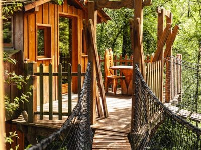 Cabane dans les arbres avec un pont suspendu, entourée de verdure luxuriante.