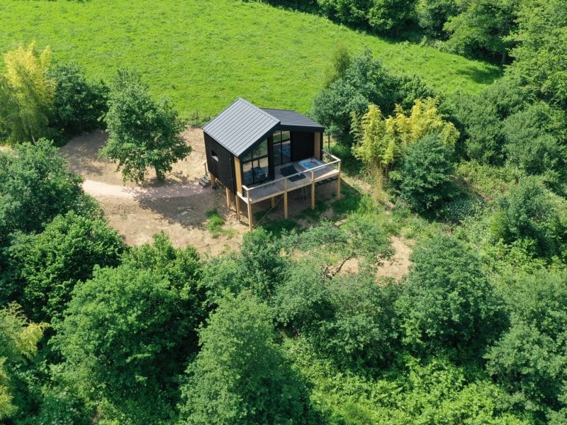 Cabane moderne en bois, nichée au cœur de la verdure, avec terrasse surplombant la nature.