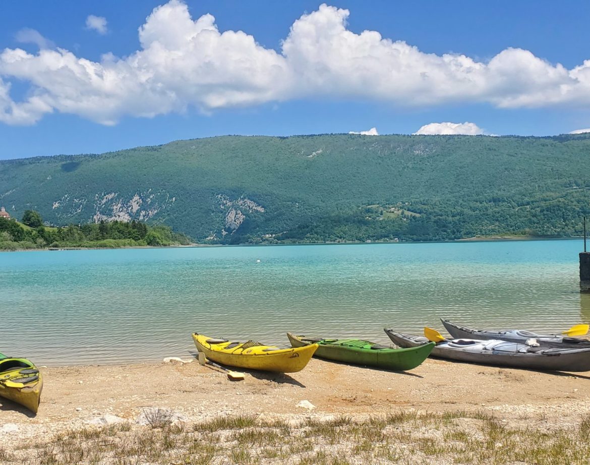 Canoës colorés sur la plage d'un lac turquoise, entouré de montagnes verdoyantes.