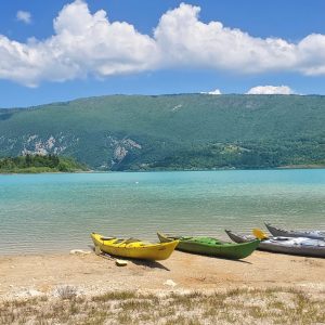 Canoës colorés sur la plage d'un lac turquoise, entouré de montagnes verdoyantes.