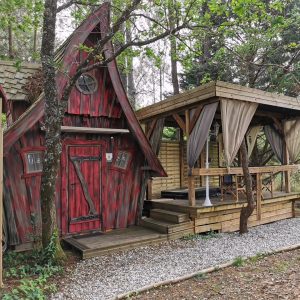 Charmante cabane en bois rouge avec terrasse couverte, entourée d'arbres verdoyants.