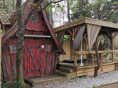 Charmante cabane en bois rouge avec terrasse couverte, entourée d'arbres verdoyants.