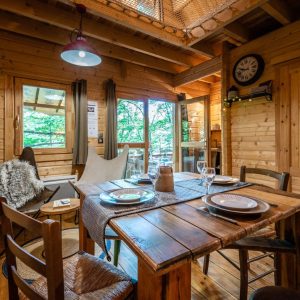 Cabane en bois chaleureuse avec table en bois, chaises confortables et vue sur la nature.