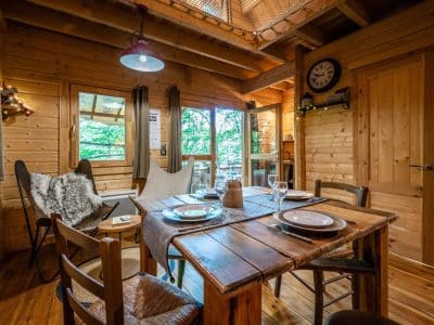 Cabane en bois chaleureuse avec table en bois, chaises confortables et vue sur la nature.