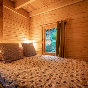 Chalet en bois chaleureux avec lit douillet et vue sur la nature à travers la fenêtre.