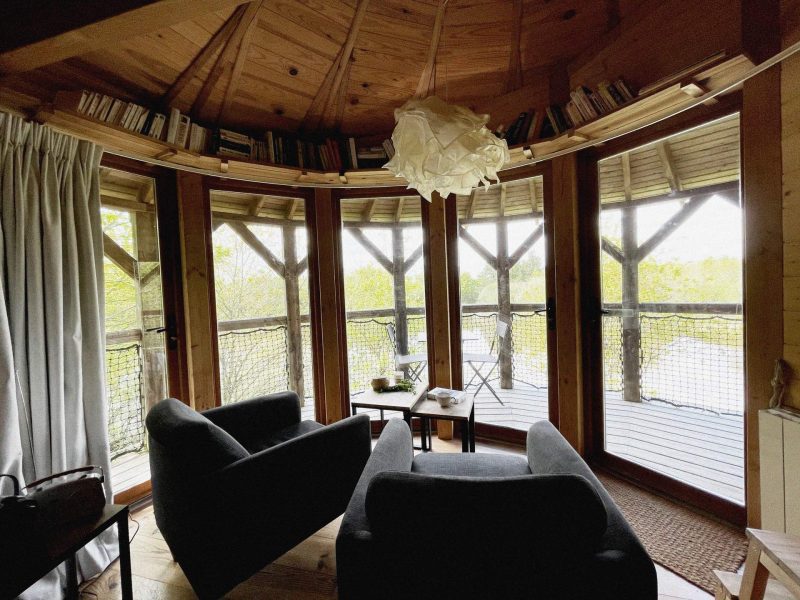 Cabane en bois avec vue panoramique, fauteuils confortables et lumière naturelle.