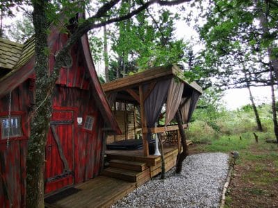 Cabane en bois rouge avec terrasse surélevée, entourée d'arbres verdoyants.