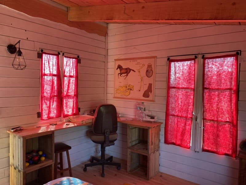 Cabane en bois avec fenêtres à rideaux rouges et un bureau en bois.