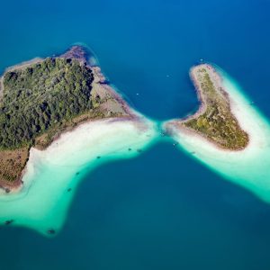 Vue aérienne de cabanes sur pilotis entourées d'eaux turquoise et de plages de sable fin.