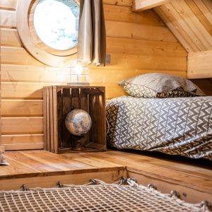 Cabane en bois chaleureuse avec lit douillet et fenêtre ronde, ambiance cocooning.