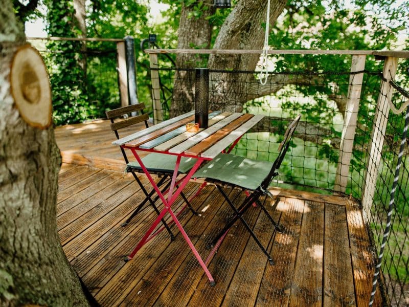 Cabane dans les arbres avec une terrasse en bois et une table pour deux.