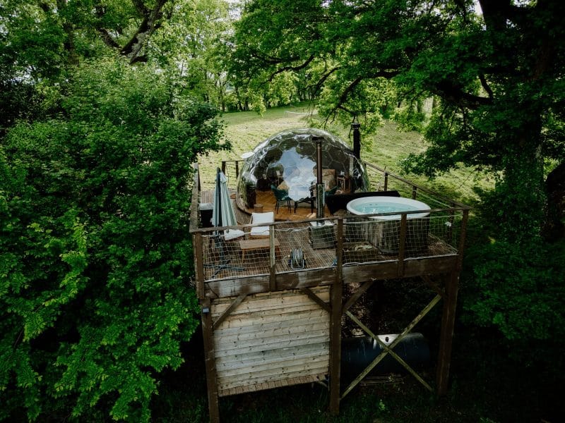 Dôme transparent surélevé, entouré darbres, avec jacuzzi sur la terrasse.