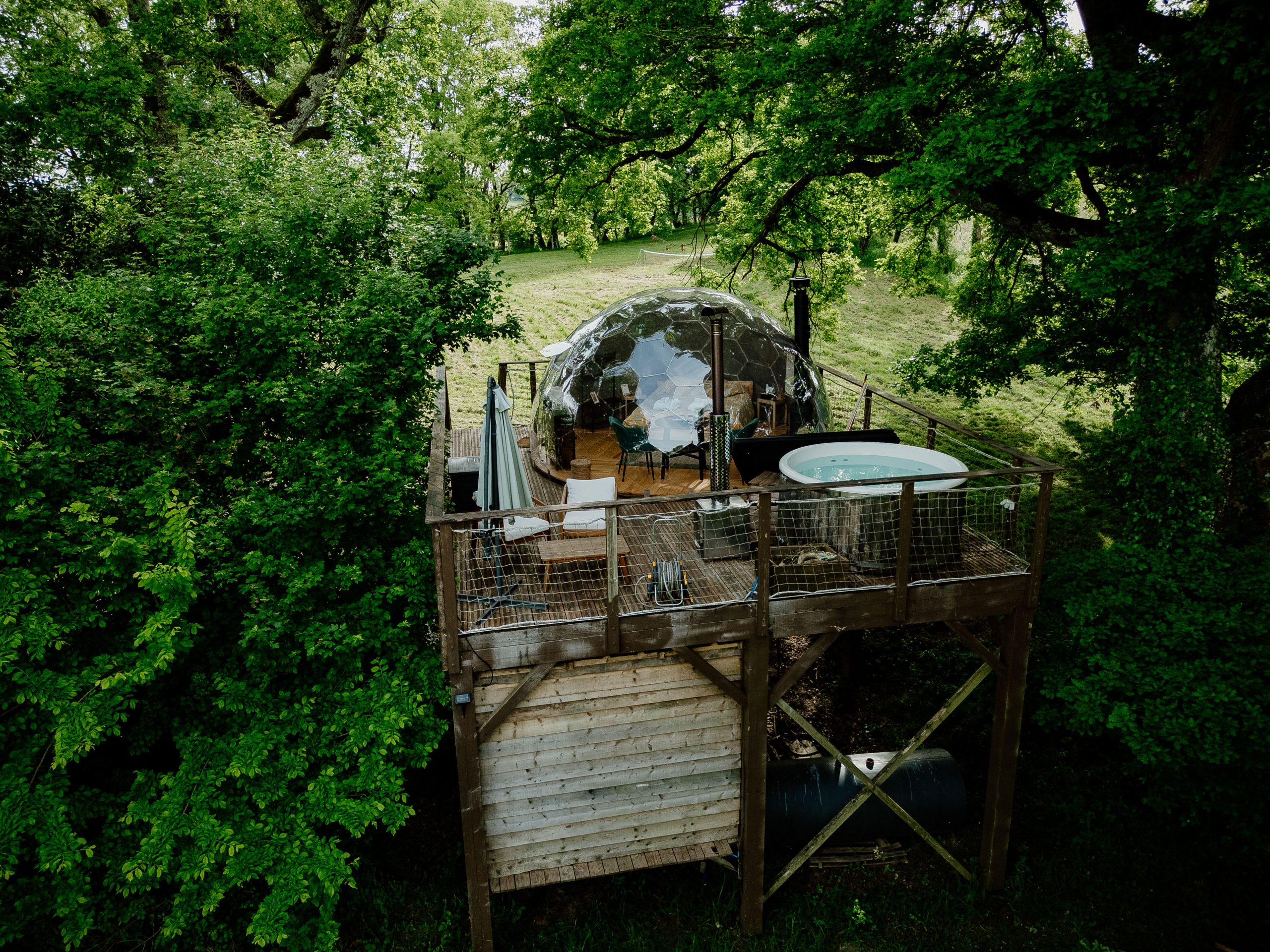 Dôme transparent perché dans les arbres, avec jacuzzi et vue sur la nature environnante.