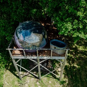 Hébergement insolite : bulle transparente perchée sur pilotis, avec jacuzzi à proximité.