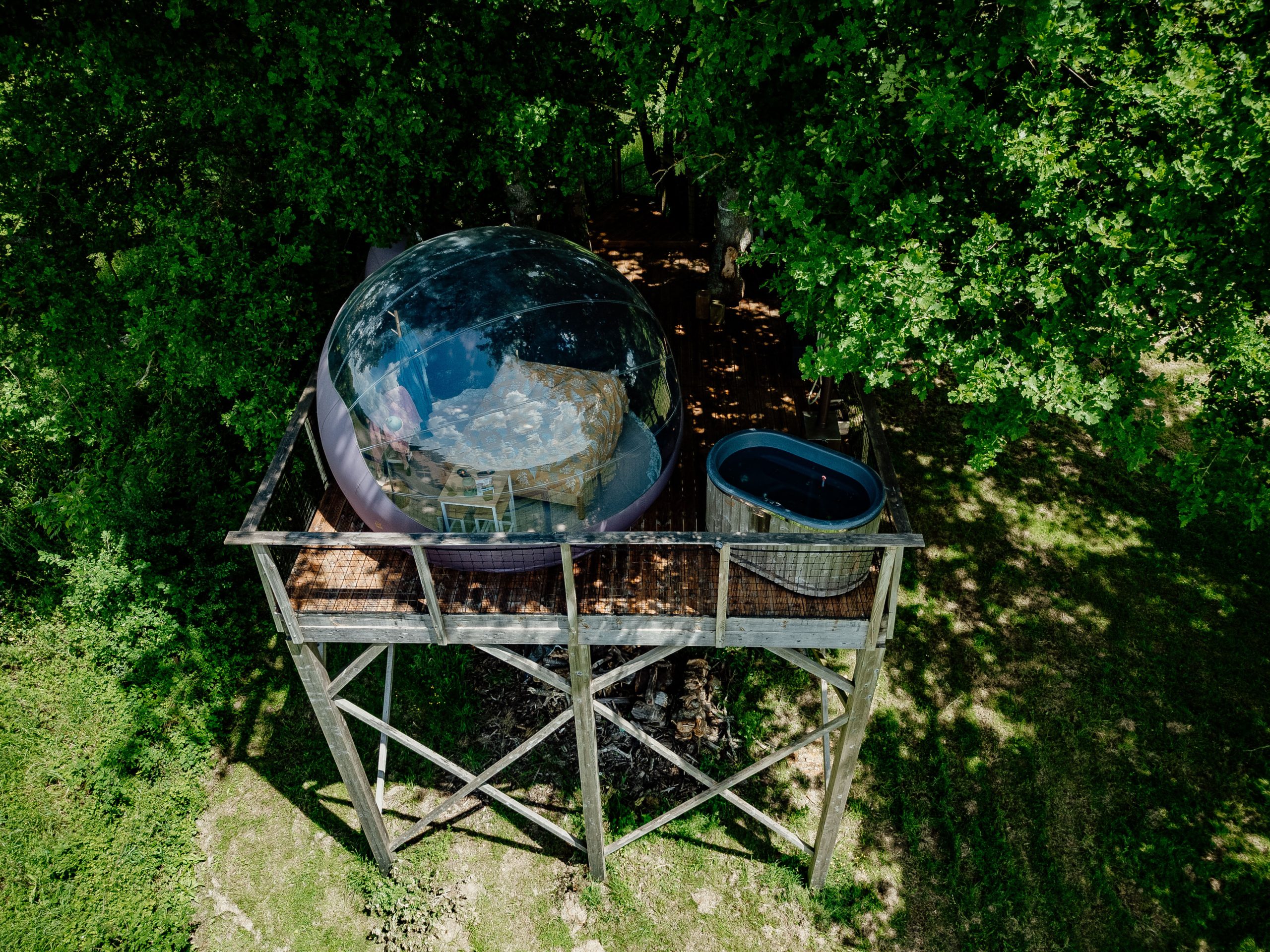 Hébergement insolite : bulle transparente perchée sur pilotis, avec jacuzzi à proximité.