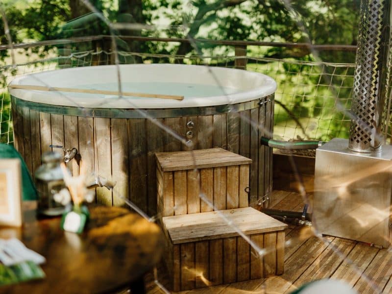 Cabane avec jacuzzi en bois, entourée de verdure et dune ambiance naturelle.