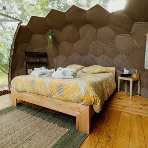 Chambre dans une cabane hexagonale, avec un lit douillet et des murs en bois naturel.