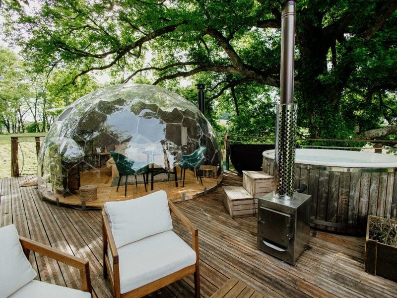 Hébergement insolite : bulle transparente en bois, jacuzzi et vue sur la nature environnante.