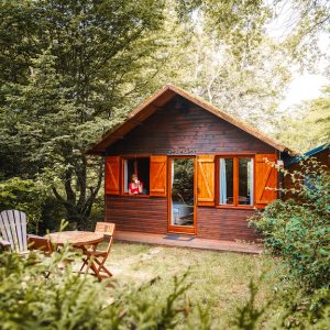 Charmant chalet en bois avec volets ouverts, entouré de verdure et d'un coin repas extérieur.