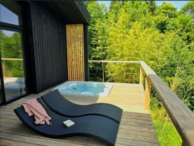 Hébergement insolite : chalet moderne avec jacuzzi sur la terrasse, entouré de verdure.