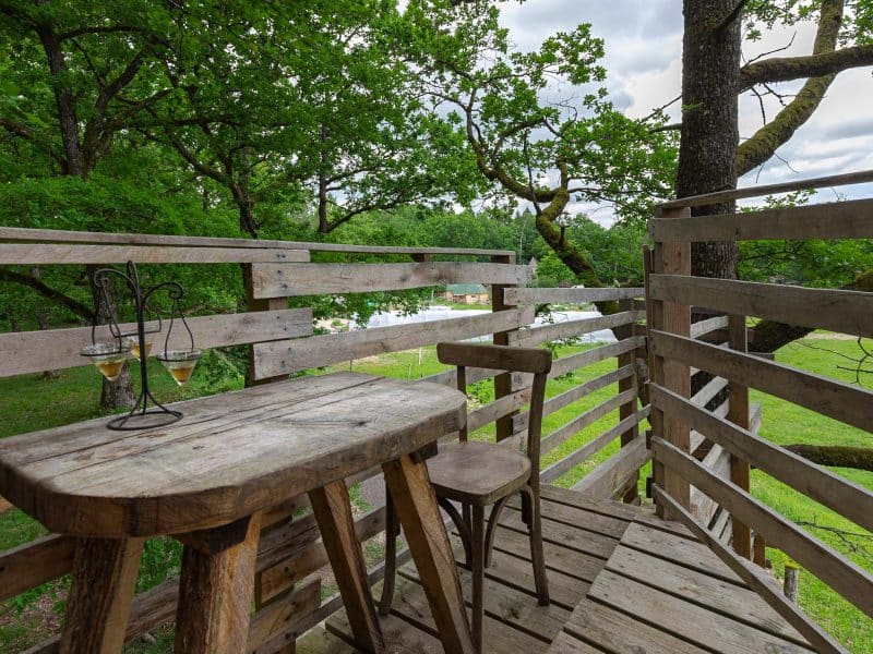 Cabane perchée avec terrasse en bois, vue sur la nature verdoyante.