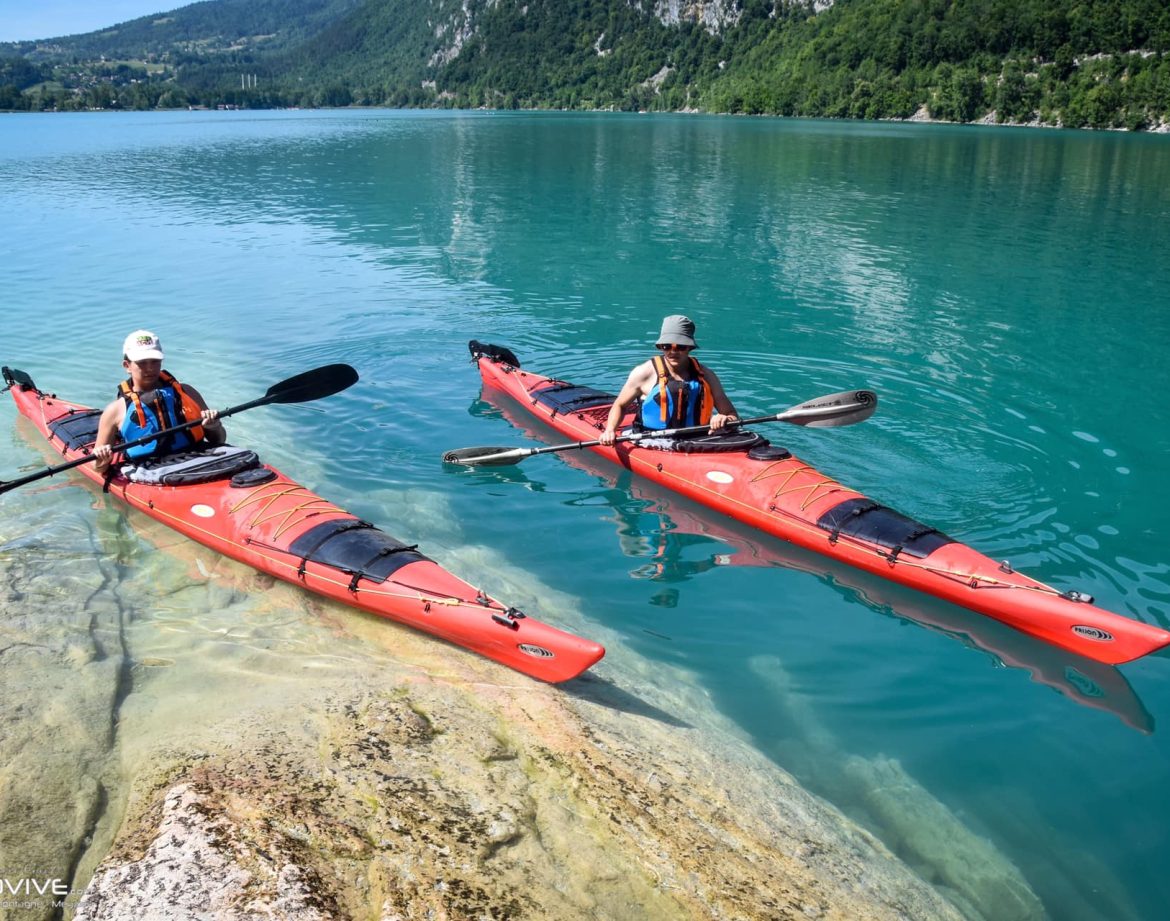 Deux kayaks rouges glissent sur les eaux turquoise d'un lac entouré de montagnes verdoyantes.