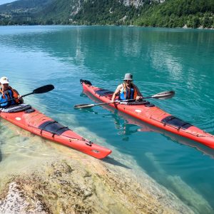 Deux kayaks rouges glissent sur les eaux turquoise d'un lac entouré de montagnes verdoyantes.