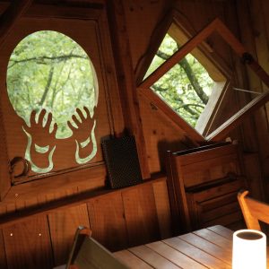 Cabane en bois avec fenêtres originales, décorée de mains sculptées, ambiance chaleureuse.