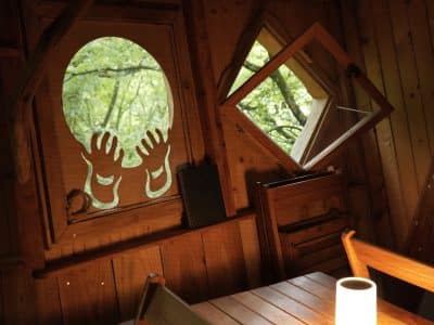 Cabane en bois avec fenêtres originales, décorée de mains sculptées, ambiance chaleureuse.