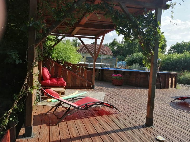 Chalet en bois avec terrasse ensoleillée et fauteuils confortables.